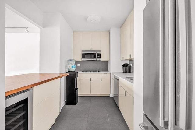 kitchen featuring dark tile patterned flooring, appliances with stainless steel finishes, cream cabinetry, beverage cooler, and decorative backsplash