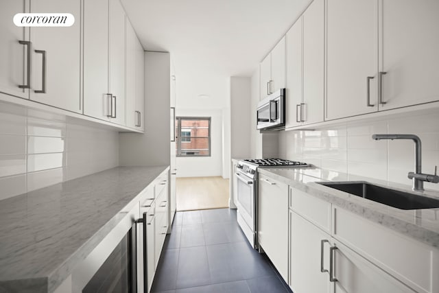 kitchen with light stone countertops, sink, backsplash, stainless steel appliances, and white cabinets