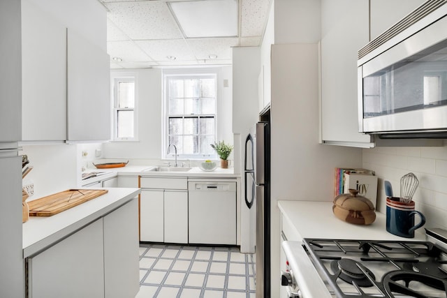 kitchen with a drop ceiling, white cabinets, sink, tasteful backsplash, and appliances with stainless steel finishes