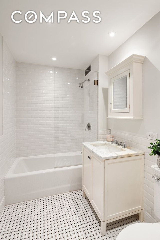 full bathroom featuring tiled shower / bath, vanity, tile walls, and toilet