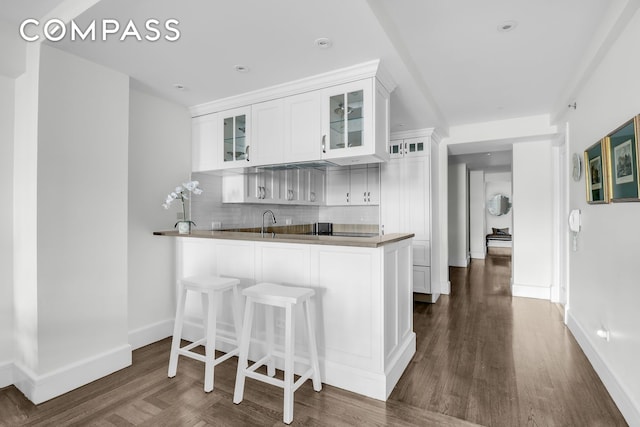 kitchen with dark wood-type flooring, tasteful backsplash, kitchen peninsula, and white cabinets