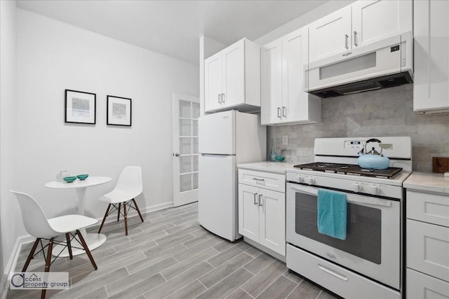 kitchen featuring light wood-type flooring, white appliances, white cabinetry, and backsplash