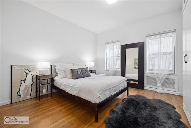 bedroom with multiple windows, radiator heating unit, and hardwood / wood-style flooring