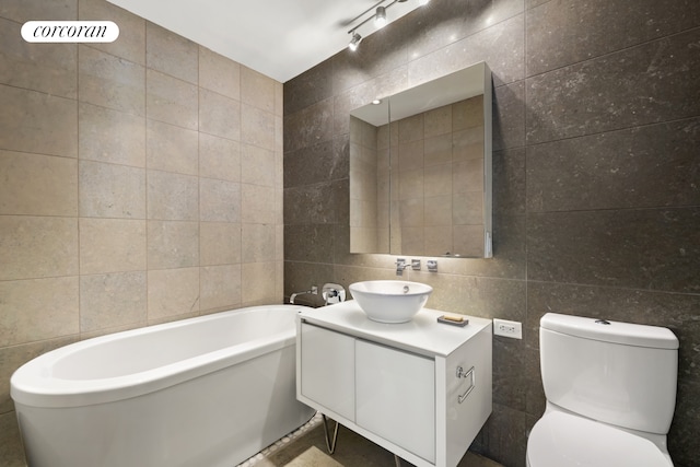 bathroom featuring tile walls, vanity, rail lighting, toilet, and a tub to relax in