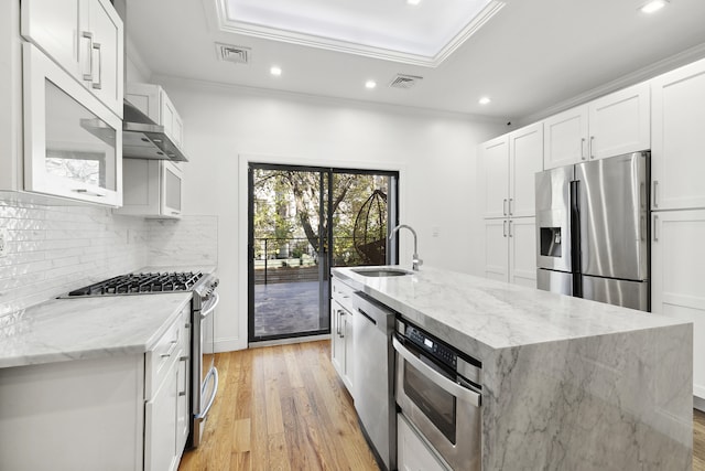 kitchen with appliances with stainless steel finishes, light stone countertops, light hardwood / wood-style floors, white cabinets, and a kitchen island with sink