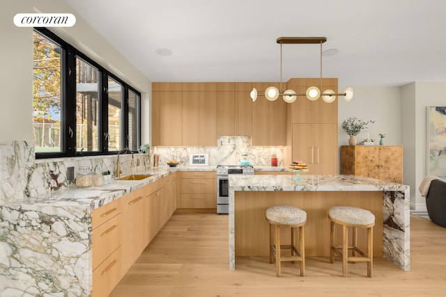 kitchen featuring gas stove, light brown cabinetry, light wood-type flooring, and sink