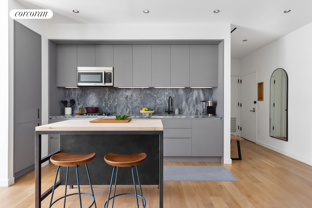 kitchen featuring decorative backsplash, light wood-type flooring, gray cabinetry, sink, and a breakfast bar area