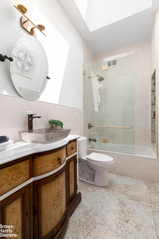 full bathroom featuring vanity, a skylight, tiled shower / bath combo, toilet, and tile walls