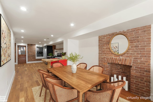 dining room with a fireplace, brick wall, and light hardwood / wood-style flooring