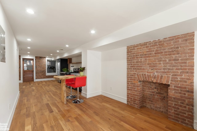 living room with a fireplace, light wood-type flooring, and brick wall