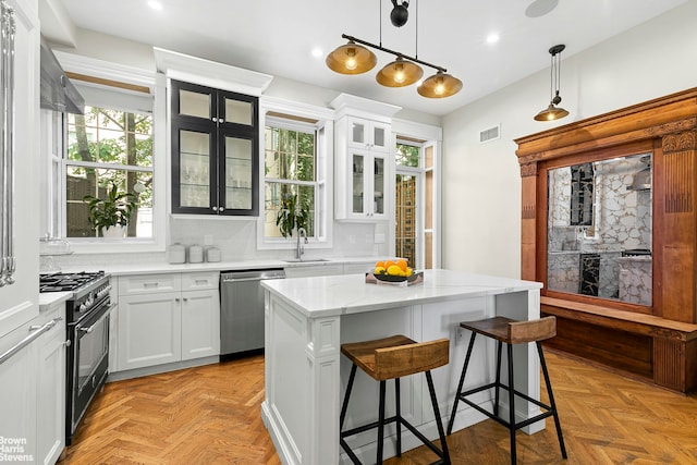 kitchen featuring appliances with stainless steel finishes, light parquet floors, a kitchen island, pendant lighting, and white cabinetry