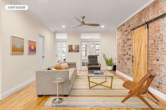 living room with a barn door, light wood-type flooring, crown molding, and brick wall