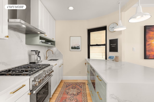 kitchen with high end range, sink, white cabinets, and wall chimney range hood