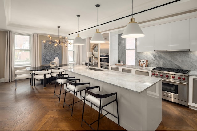 kitchen with hanging light fixtures, designer stove, a breakfast bar area, a kitchen island with sink, and white cabinets