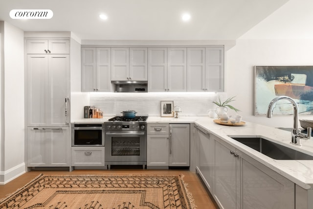 kitchen featuring light stone countertops, decorative backsplash, gray cabinetry, high end appliances, and sink