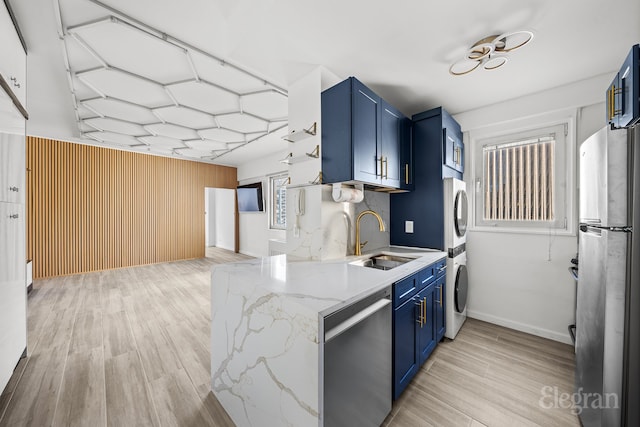 kitchen featuring sink, stainless steel appliances, light stone counters, blue cabinets, and stacked washer / dryer