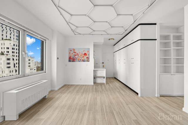 spare room featuring built in shelves, radiator heating unit, and light hardwood / wood-style flooring