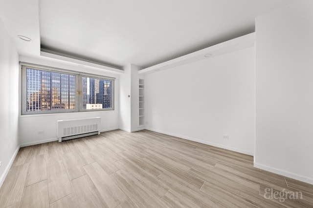 empty room featuring light wood-type flooring and radiator heating unit