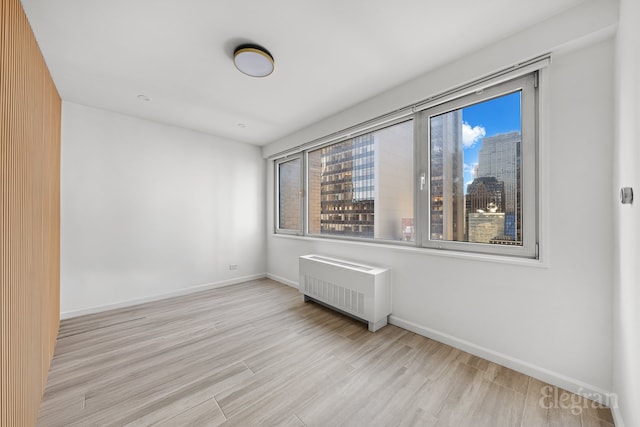 spare room with radiator heating unit and light hardwood / wood-style floors