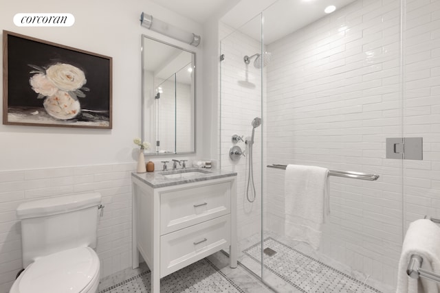 bathroom with vanity, toilet, a shower with door, and tile walls