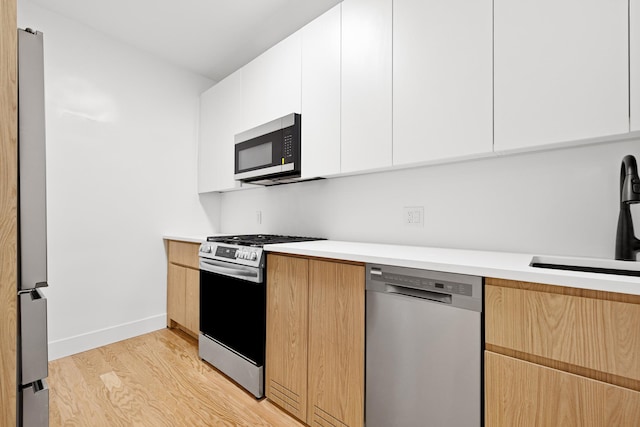 kitchen featuring appliances with stainless steel finishes, light hardwood / wood-style flooring, white cabinetry, and sink