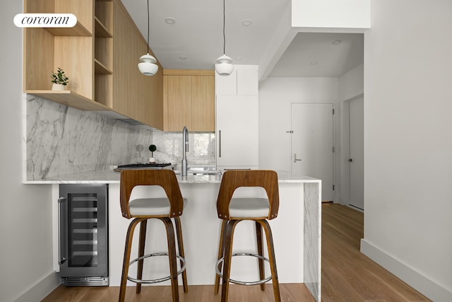 kitchen featuring wine cooler, light stone counters, kitchen peninsula, hardwood / wood-style floors, and decorative light fixtures