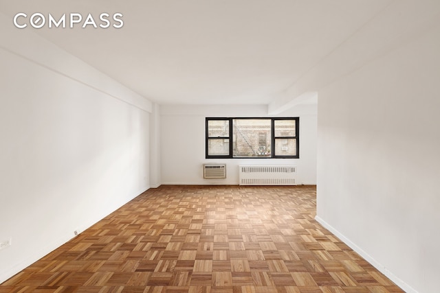 spare room featuring an AC wall unit, radiator heating unit, and light parquet floors