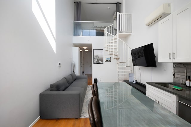 kitchen featuring white cabinets, sink, stainless steel dishwasher, light hardwood / wood-style floors, and a wall unit AC