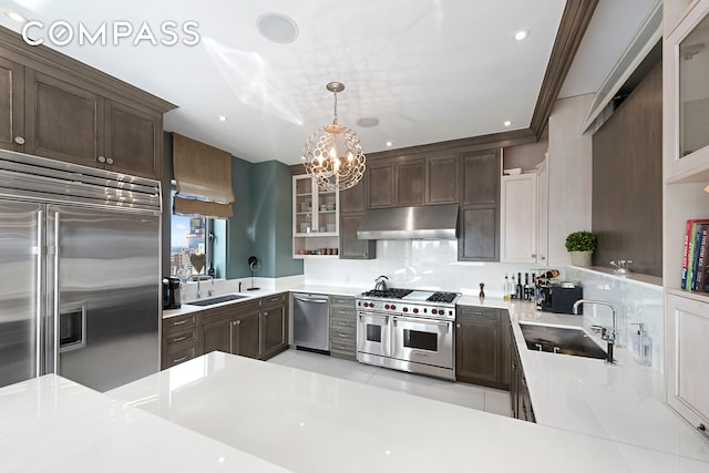 kitchen featuring pendant lighting, premium appliances, kitchen peninsula, and sink