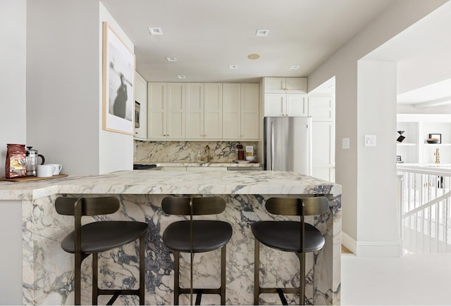 kitchen featuring a kitchen breakfast bar, decorative backsplash, appliances with stainless steel finishes, light stone counters, and kitchen peninsula