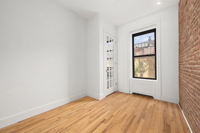 empty room with light wood-type flooring and brick wall