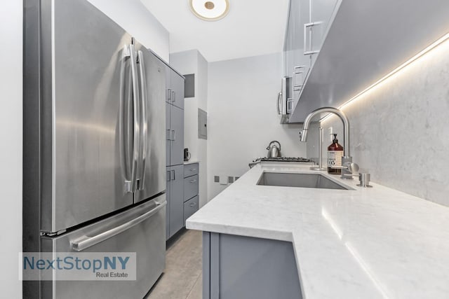 kitchen featuring gray cabinets, stainless steel fridge, light stone counters, and sink