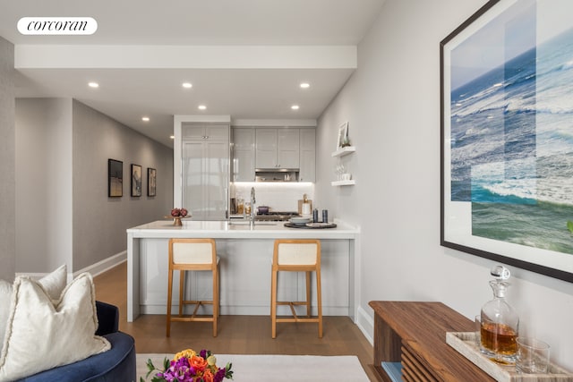 interior space featuring kitchen peninsula, decorative backsplash, sink, and dark hardwood / wood-style floors