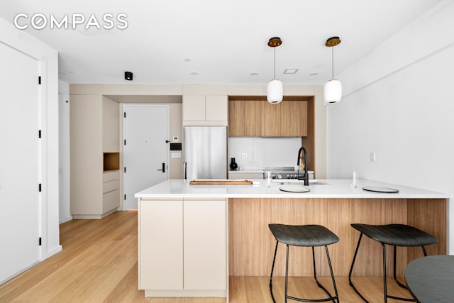 kitchen featuring sink, pendant lighting, white cabinets, light hardwood / wood-style floors, and built in fridge