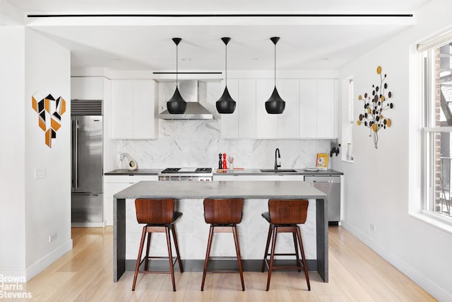 kitchen featuring pendant lighting, wall chimney range hood, sink, appliances with stainless steel finishes, and white cabinetry