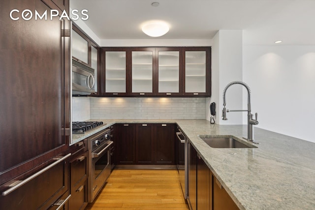 kitchen with tasteful backsplash, light stone counters, stainless steel appliances, sink, and light hardwood / wood-style floors