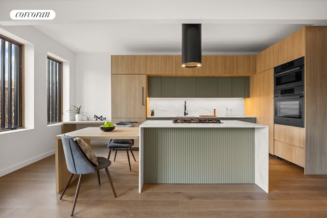 kitchen featuring double oven, light hardwood / wood-style floors, a kitchen island, and stainless steel gas cooktop