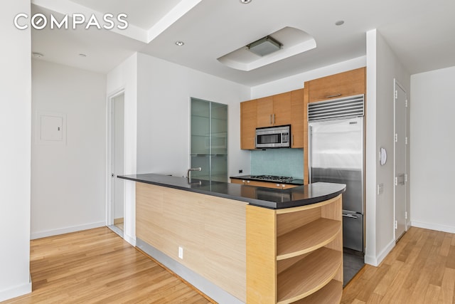 kitchen with kitchen peninsula, backsplash, stainless steel appliances, and light hardwood / wood-style flooring