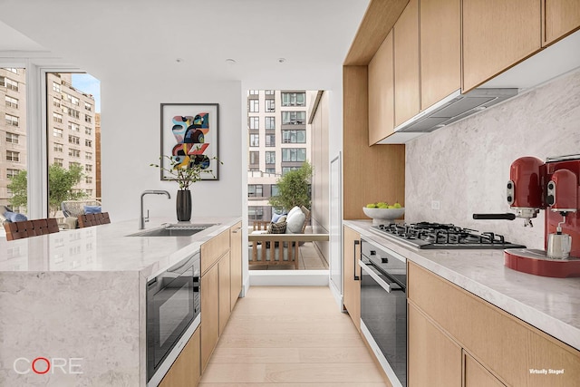 kitchen featuring sink, light brown cabinetry, tasteful backsplash, light hardwood / wood-style floors, and stainless steel appliances