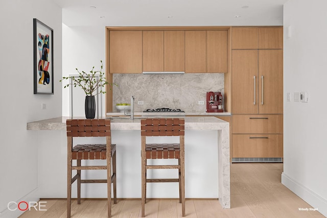 kitchen with tasteful backsplash, light stone counters, a kitchen bar, and light hardwood / wood-style floors