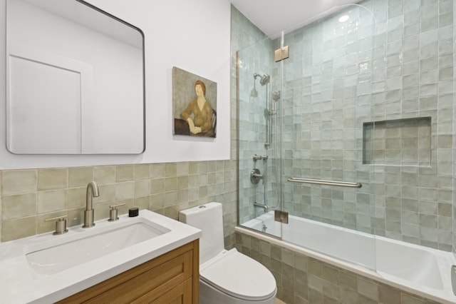 full bathroom featuring combined bath / shower with glass door, vanity, toilet, and tile walls