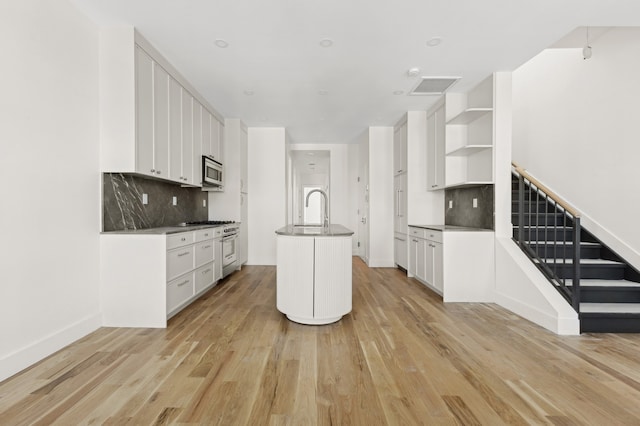 kitchen featuring tasteful backsplash, stainless steel appliances, a center island with sink, light hardwood / wood-style flooring, and white cabinetry