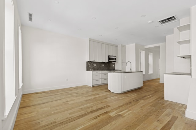 kitchen featuring backsplash, a kitchen island with sink, sink, light hardwood / wood-style flooring, and white cabinetry