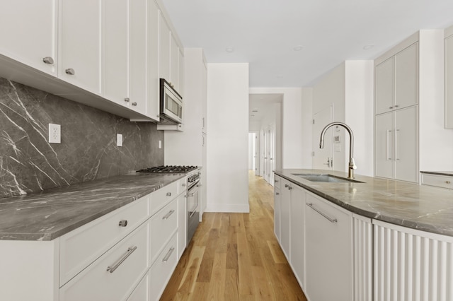 kitchen with dark stone counters, white cabinets, sink, light hardwood / wood-style flooring, and stainless steel appliances