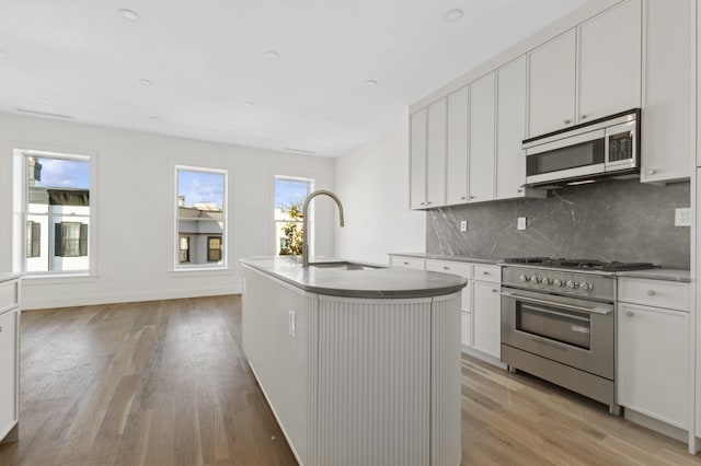 kitchen with stainless steel appliances, sink, a center island with sink, light hardwood / wood-style flooring, and white cabinetry