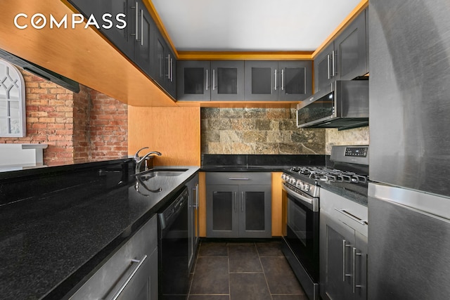 kitchen with sink, dark tile patterned floors, brick wall, decorative backsplash, and appliances with stainless steel finishes