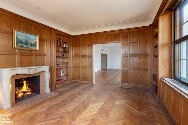 unfurnished living room featuring a fireplace, dark parquet flooring, built in features, and wood walls