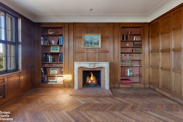 unfurnished room with built in shelves, wood walls, parquet floors, and a brick fireplace