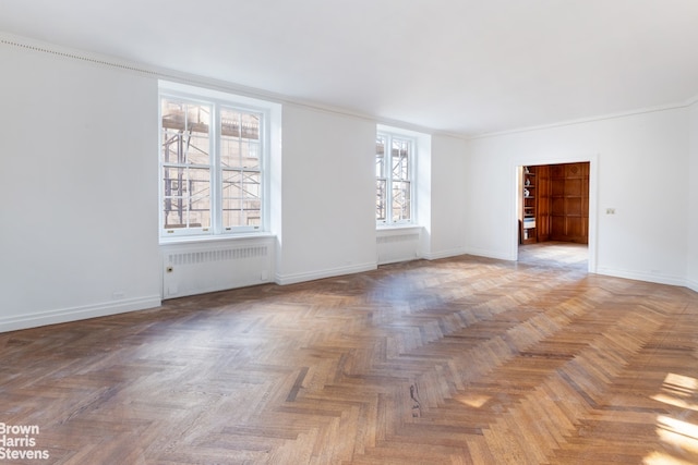 unfurnished room featuring a wealth of natural light, radiator heating unit, parquet floors, and crown molding