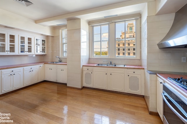 kitchen featuring stainless steel oven, wall chimney exhaust hood, decorative backsplash, light wood-type flooring, and white cabinetry